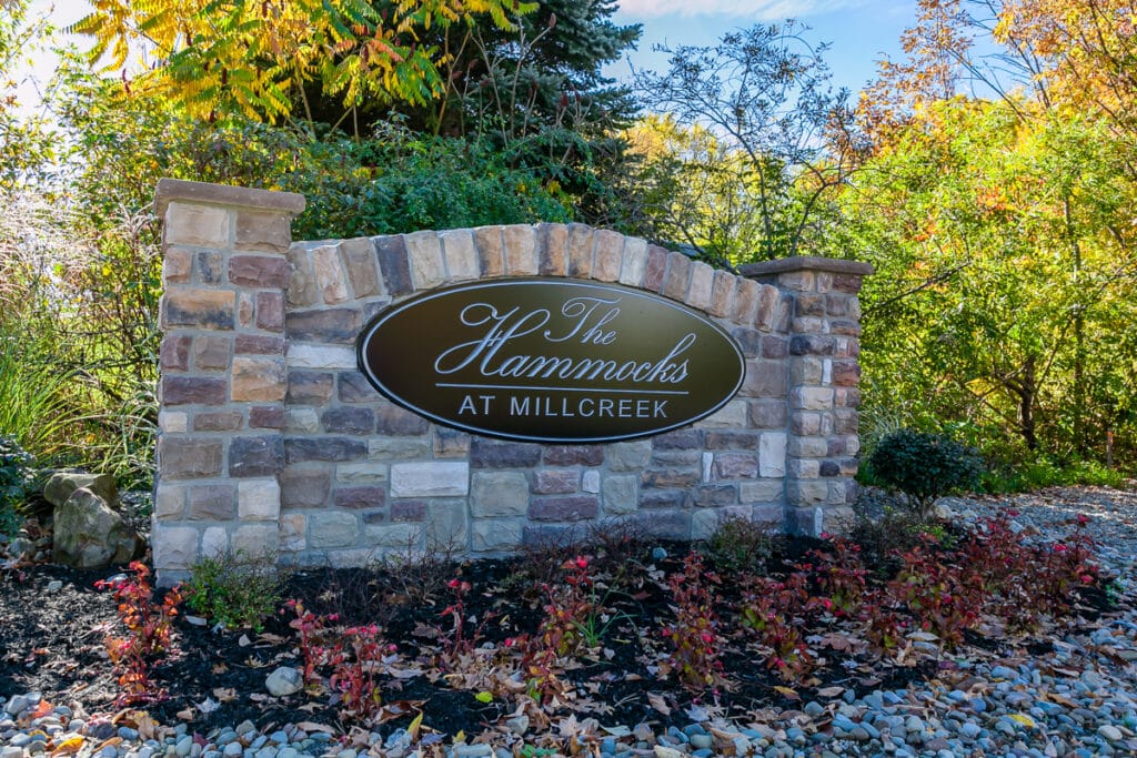 A stone sign with "The Hammocks at Millcreek" on it, surrounded by autumn foliage and landscaping.