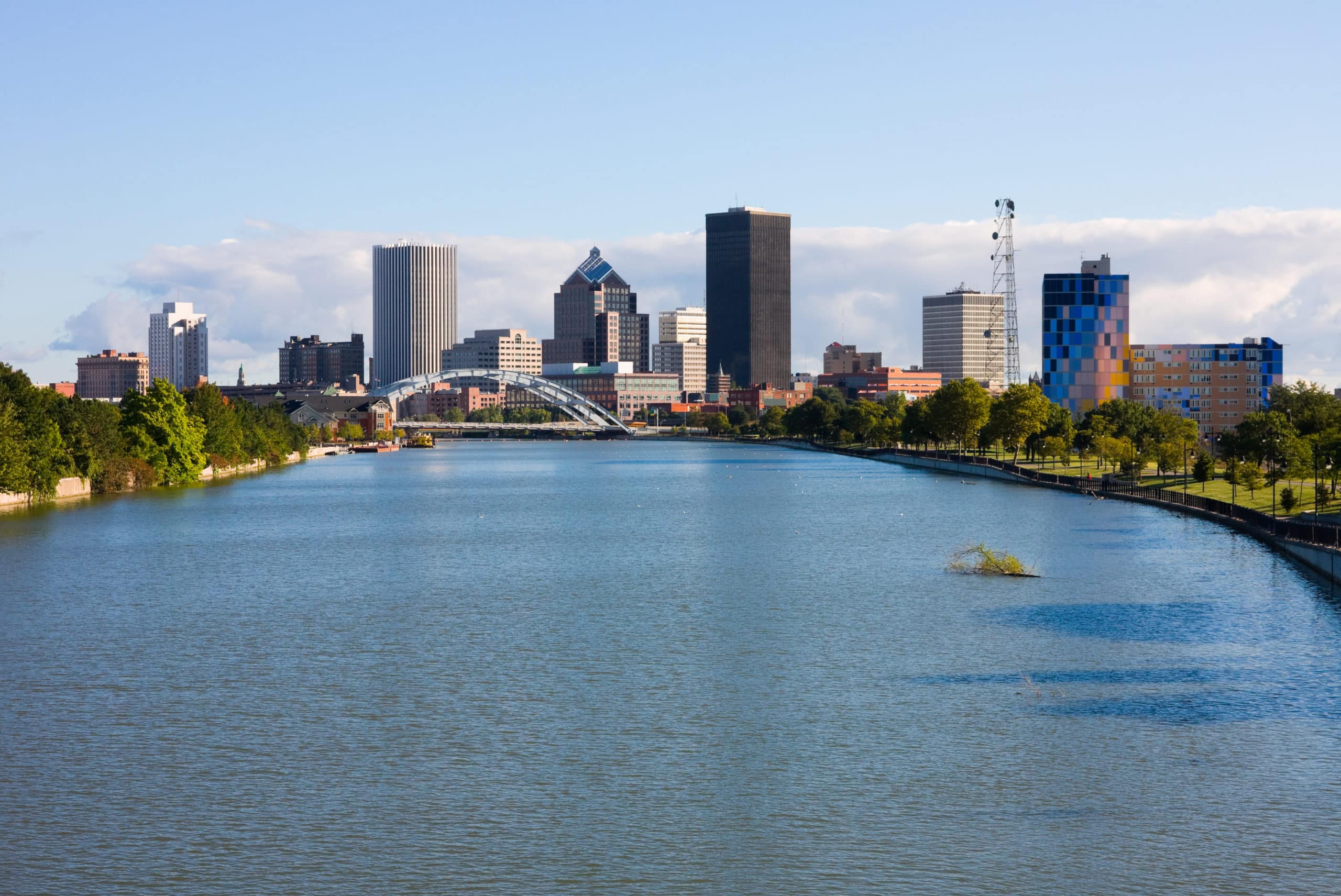 City skyline with tall buildings alongside a wide river on a clear day.