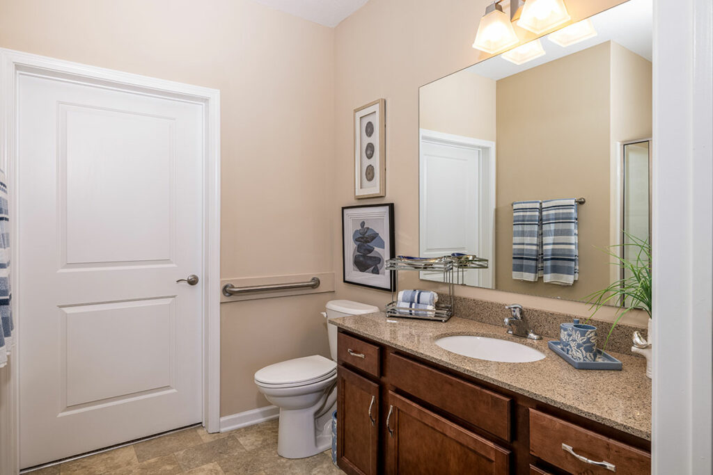 Modern apartment bathroom with maple cabinetry, quartz countertops, and ceramic tile flooring.