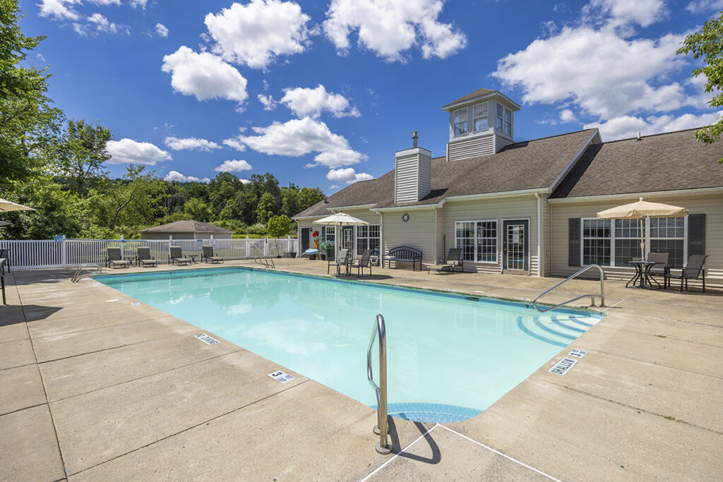 View of the clubhouse, inground pool, and sundeck at WoodsEdge Apartment Homes in Painted Post, NY, showcasing modern apartments for rent with luxurious amenities.