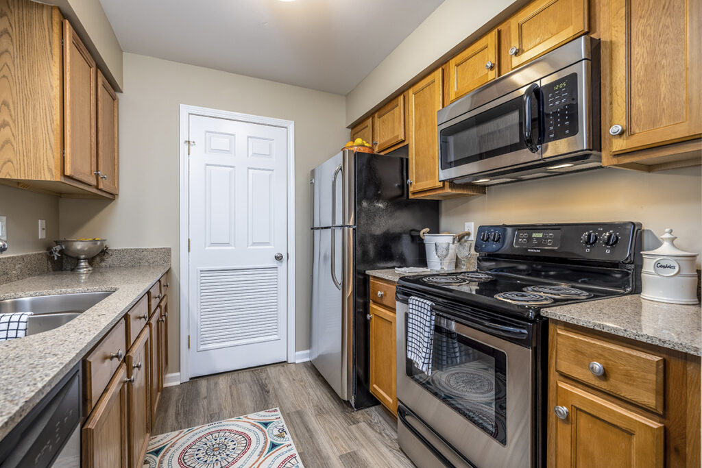 A compact kitchen featuring stainless steel appliances, quartz countertops, and LVP flooring, designed for efficiency and style.