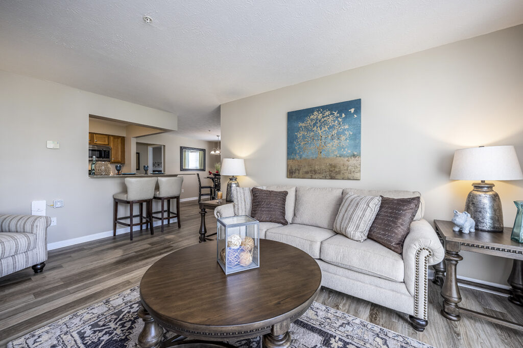 Spacious and bright living room with luxury vinyl plank flooring, offering views into the modern kitchen and breakfast bar area at The Hammocks at Orchard Park.