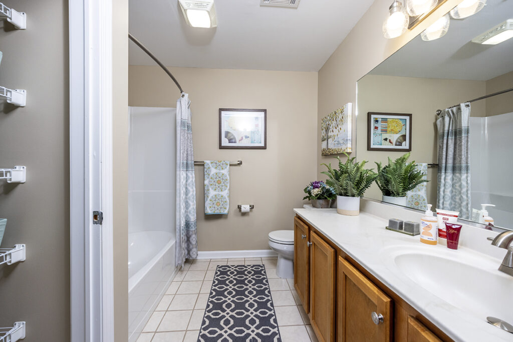 Bathroom featuring tile flooring, a large vanity with ample counter space, a tub, and a small closet for additional storage at The Hammocks at Orchard Park.