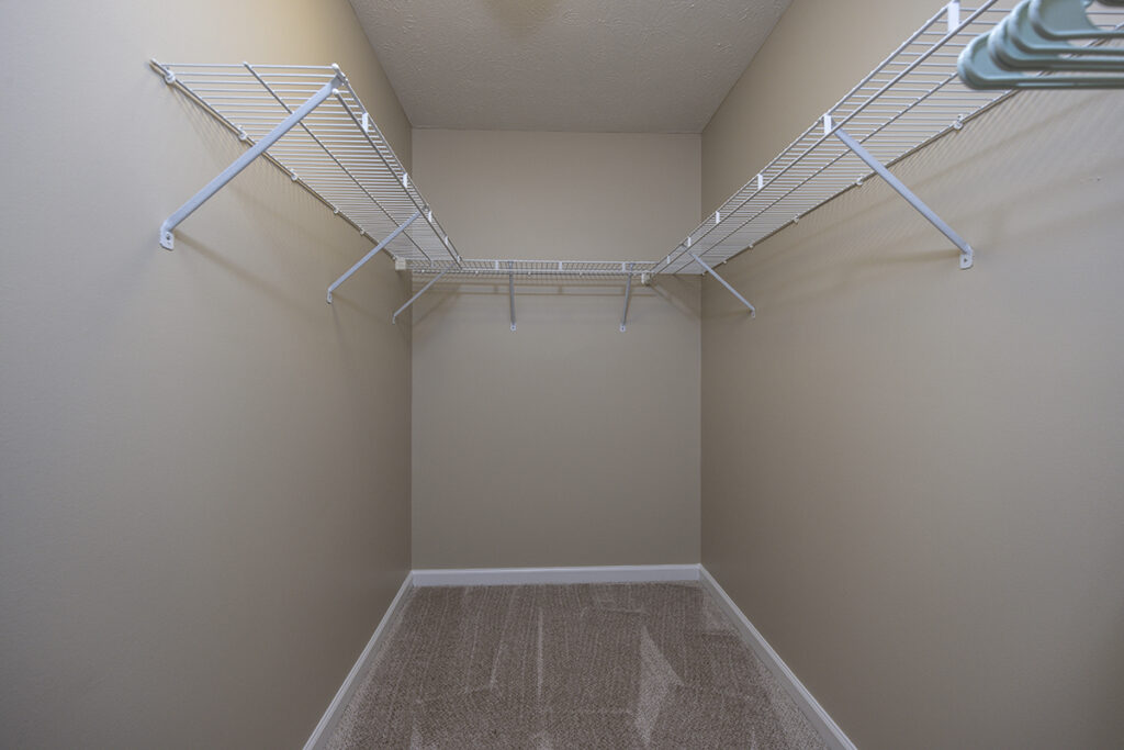 Spacious walk-in closet featuring soft carpeting and built-in storage shelves, offering plenty of room for organization at The Hammocks at Orchard Park.