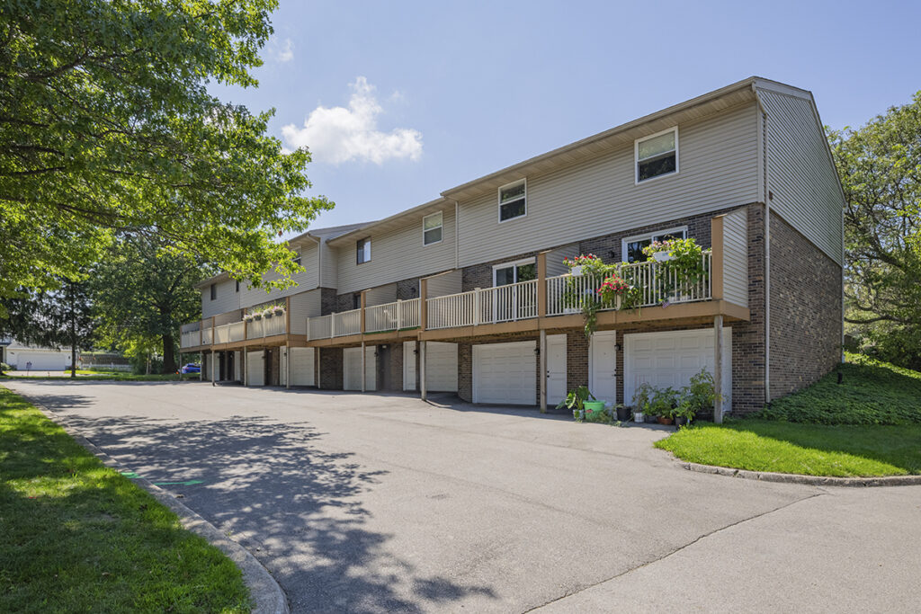 A serene view of the back side of townhomes, featuring private garages, secondary private entrances, and updated private patios. The scene highlights a comfortable and stylish living space with modern amenities.