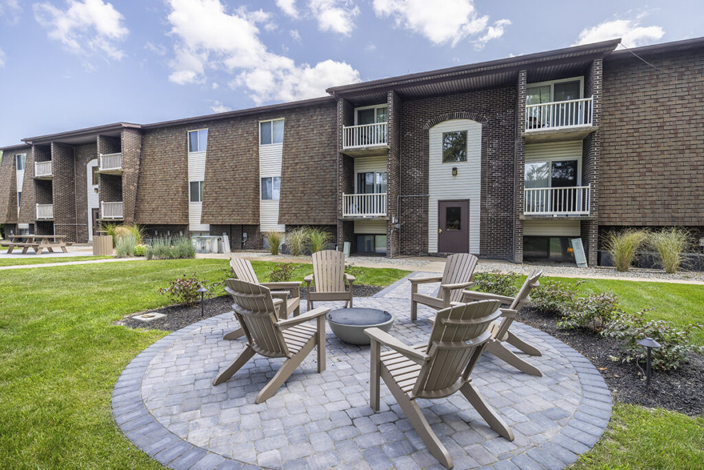 Brand new firepit with Adirondack chair seating on a stone concrete pad, surrounded by nicely maintained landscaping in the courtyard.