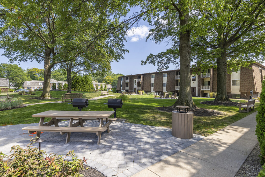 View of the courtyard showcasing beautiful mature landscaping, a picnic area, a firepit, and a nicely paved path leading through the space, creating a welcoming and well-maintained outdoor environment.