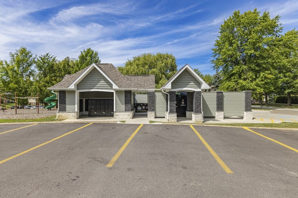 A small park building with gray siding and black accents. It has multiple doors and is set against a backdrop of trees and a playground.