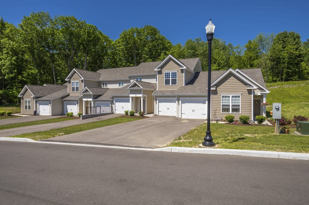 A row of modern townhouses with garages, surrounded by green trees, under a clear blue sky.