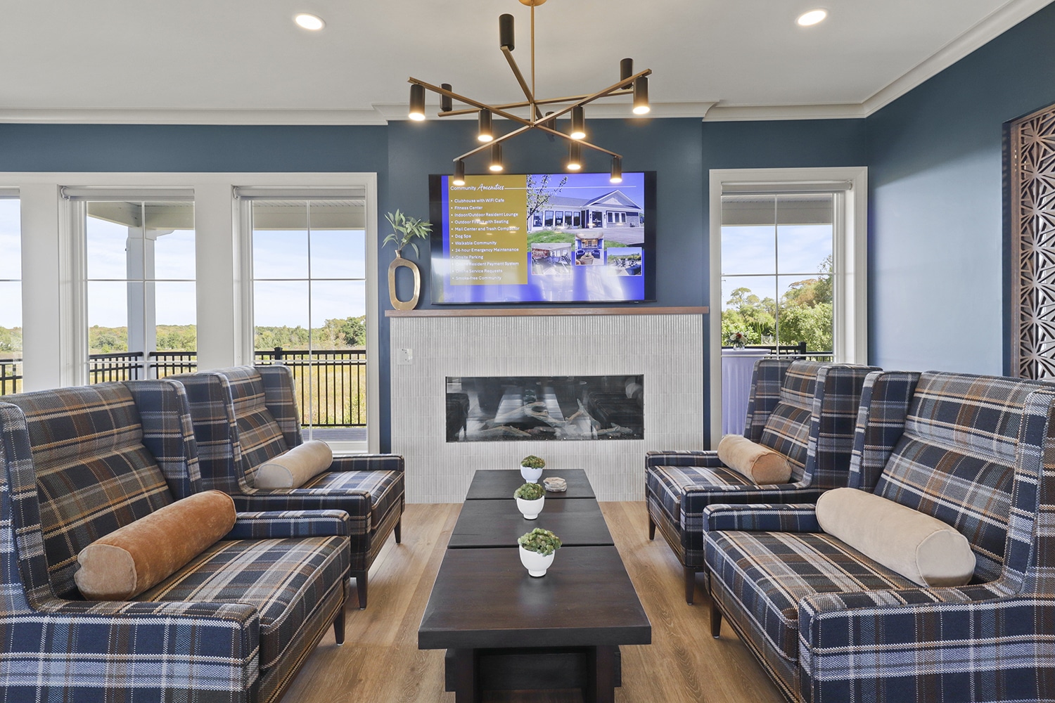 Modern living room with blue walls, plaid armchairs, a central coffee table with small potted plants, a fireplace, and a TV above showcasing real estate details for The Hammocks at Fairview.