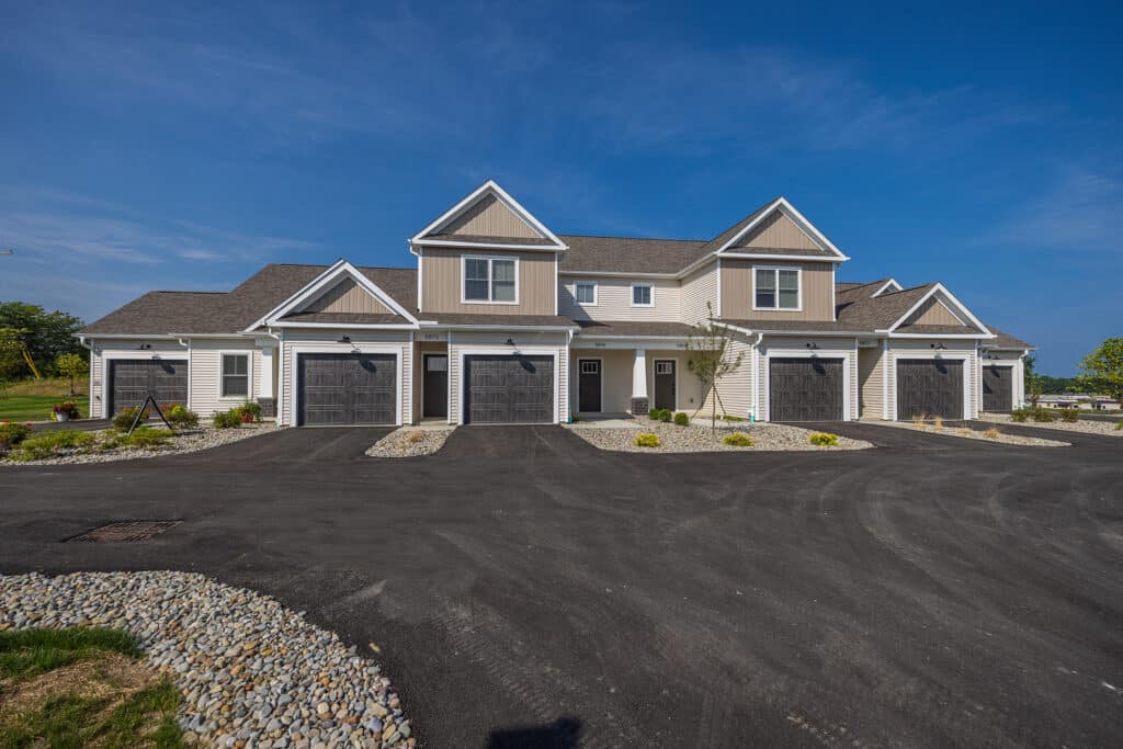 A row of modern townhouses with attached garages, gray siding, and landscaped stone areas under a clear blue sky.