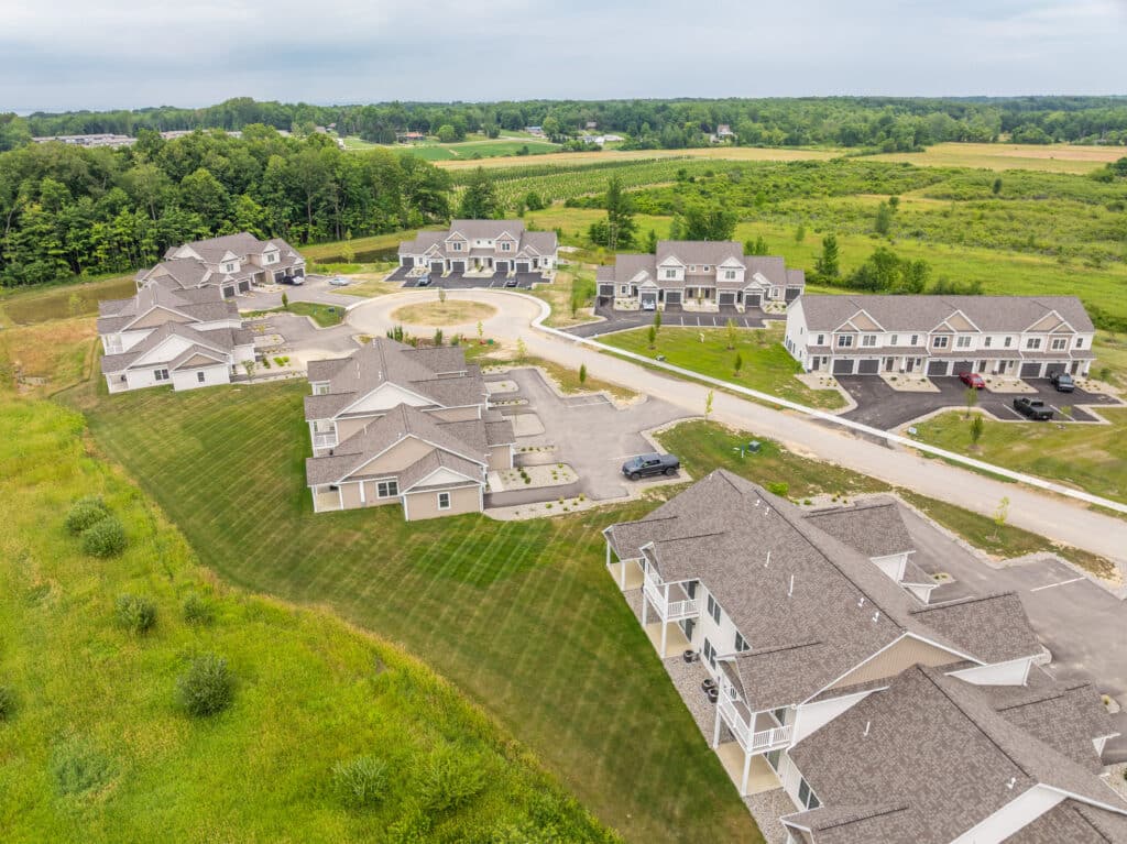 Aerial view of a The Hammocks at Fairview community showing multi-unit buildings, paved driveways, parked cars, and surrounding green fields.