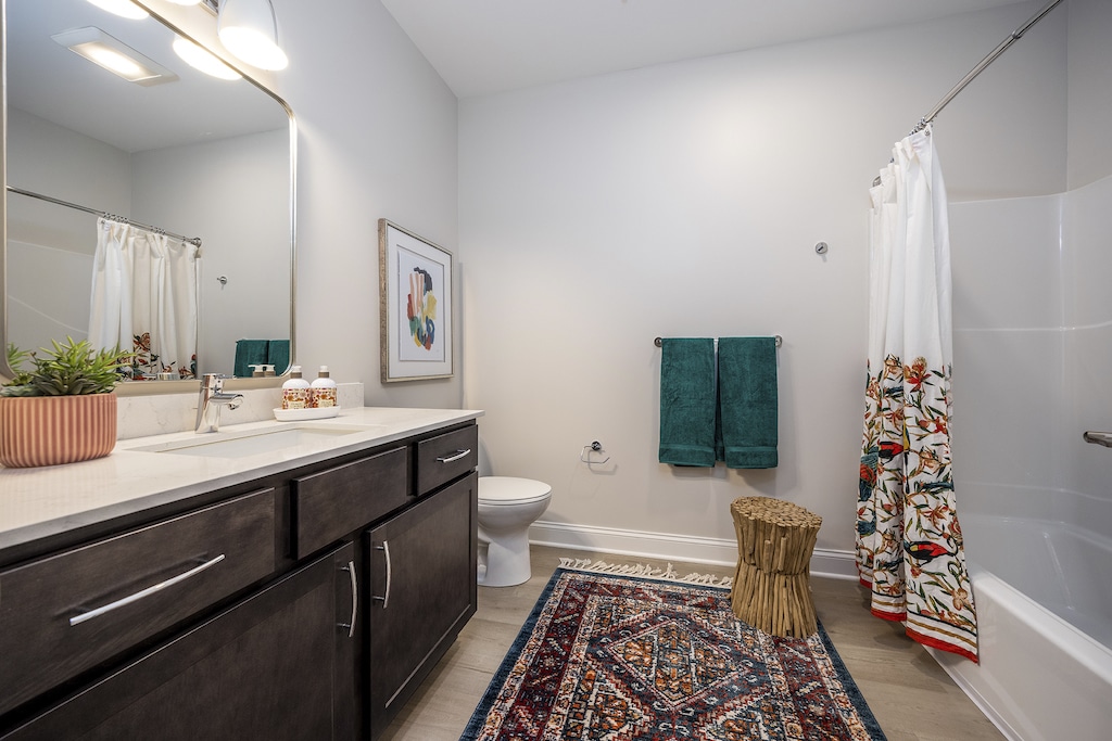 Spacious bathroom with a dark wood vanity, white countertop, and under-mount sink. A white bathtub with a colorful shower curtain and teal towels add accents. A framed artwork hangs on the wall.