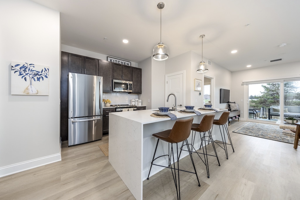 Modern kitchen featuring a sleek breakfast bar accented by pendant lights, complemented by stunning waterfall quartz countertops and modern high-end stainless steel appliances.
