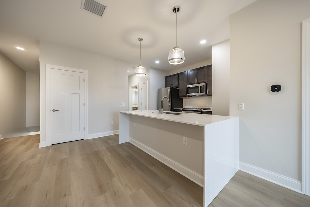 Modern kitchen featuring sleek white quartz countertops with a breakfast bar, stylish cabinetry, stainless steel appliances, and elegant LVP flooring.