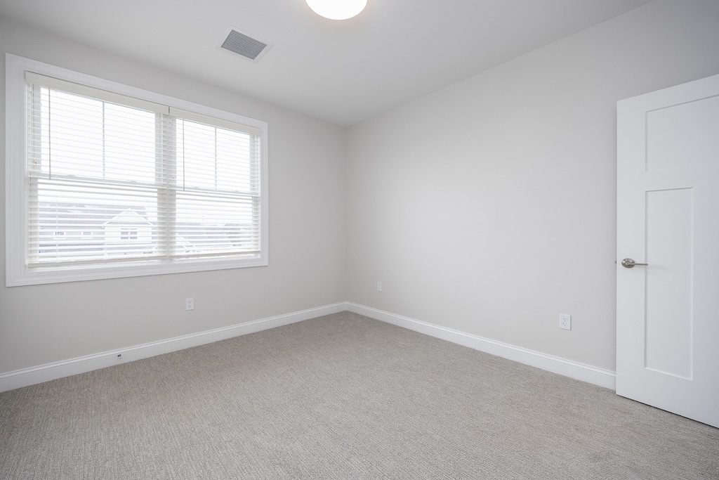 Empty room with gray carpet, white walls, a window with blinds, and a closed white door.