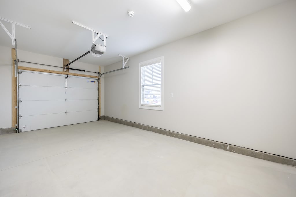 Attached empty finished garage with a closed white door, concrete floor, and a single window on the right wall.