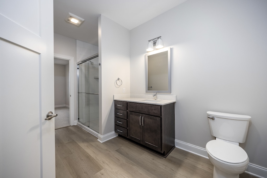 Spacious Bathroom with No-Step Shower, Tile Walls, Glass Shower Doors, LVP Flooring, and Dark Maple Cabinetry.