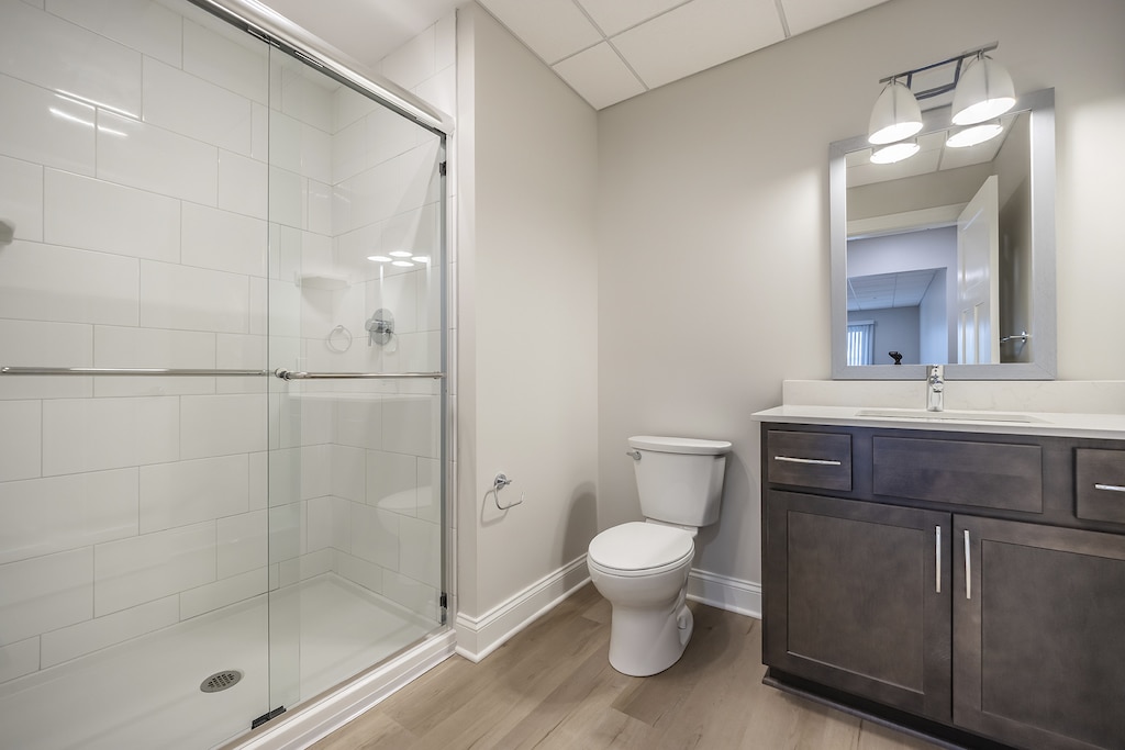 Modern bathroom with glass-enclosed white tile shower, white toilet, and dark wood vanity with white quartz countertops rectangular mirror.