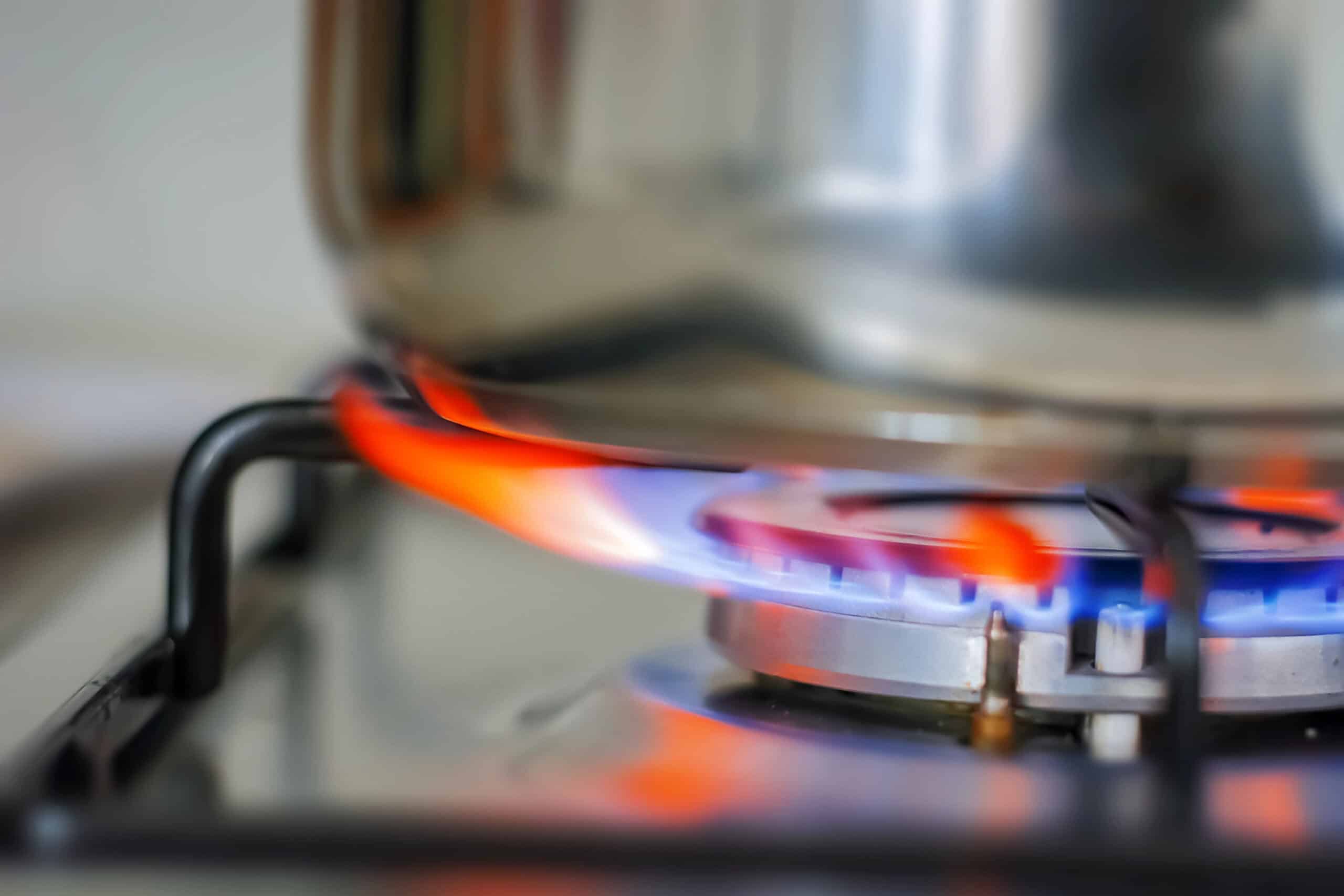 A pot on a gas stove with blue and orange flame heating the burner.