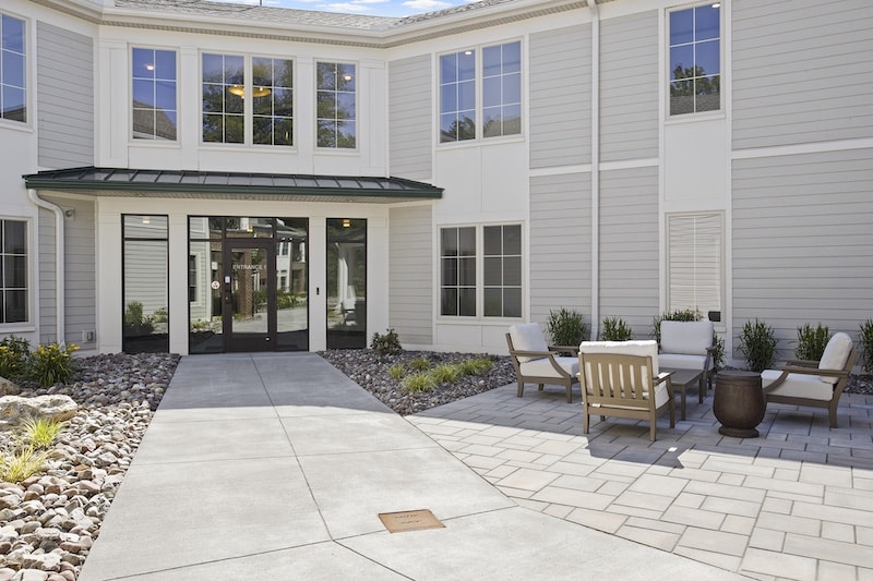 Courtyard of a modern building with beige and white exterior, featuring a patio area with seating and a walkway surrounded by landscaped stones and plants.