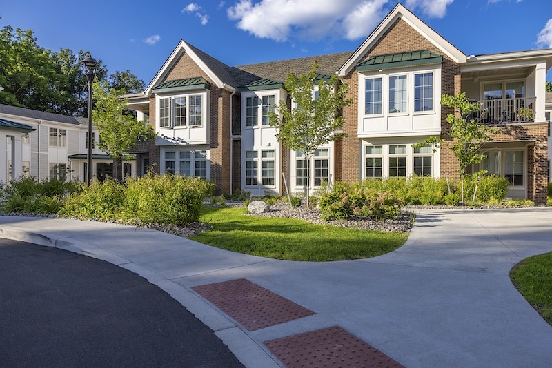 Two-story brick and white residential building with a landscaped front yard and curved walkway under a clear blue sky.