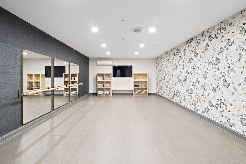 Exercise studio with mirrors, wall art, and shelves containing towels and yoga mats. A TV is mounted on the wall.