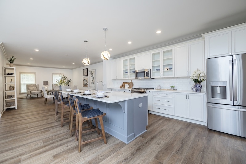 Modern kitchen and dining area with wood floors, white cabinets, stainless steel appliances, and a blue island with barstools. Dining table is set for six.
