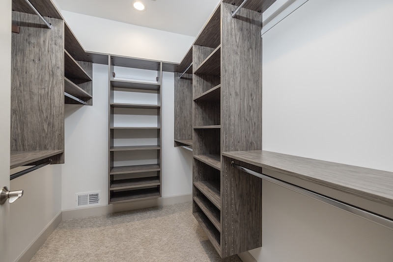Empty walk-in closet with wooden shelves, hanging rods, and carpeted floor.