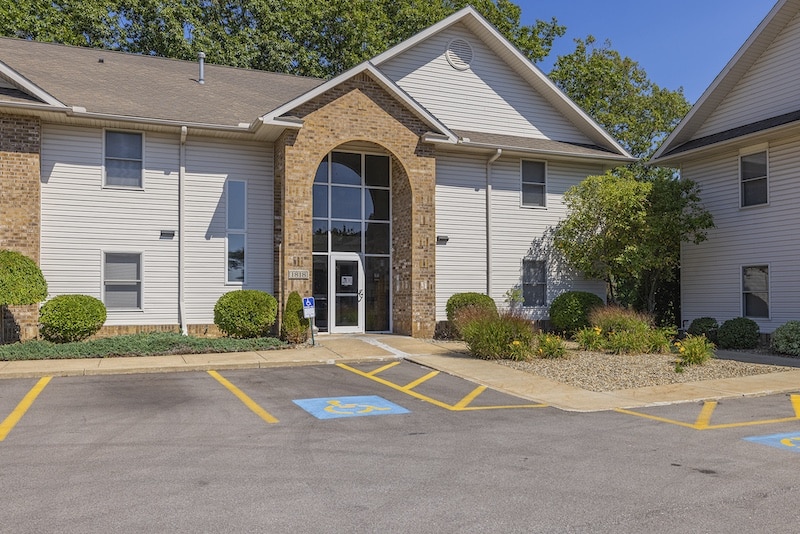 A two-story building with a brick and siding exterior, featuring a central glass entrance. Fronted by a parking lot with clearly marked accessible parking spaces.