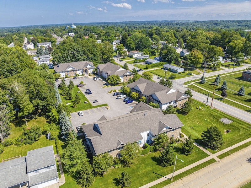 Aerial view of a suburban neighborhood with houses, green trees, and a parking area on a clear day.