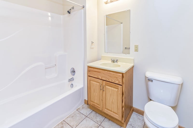 A clean bathroom with a bathtub, shower, wooden vanity with sink, mirror, and toilet on tiled floor.