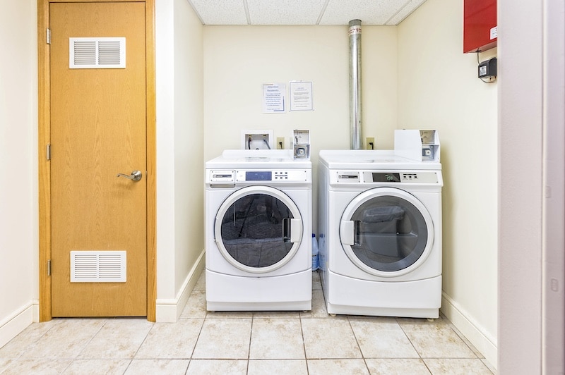 Laundry room with a front-loading washer and dryer side by side against a cream wall. A wooden door is on the left.