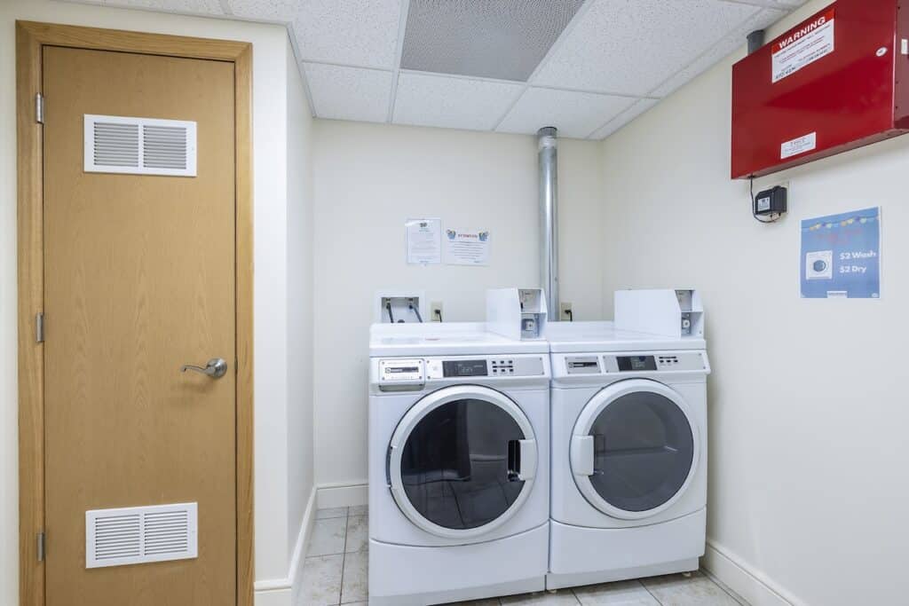 Laundry room with a washing machine and dryer side by side against the wall, next to a wooden door.