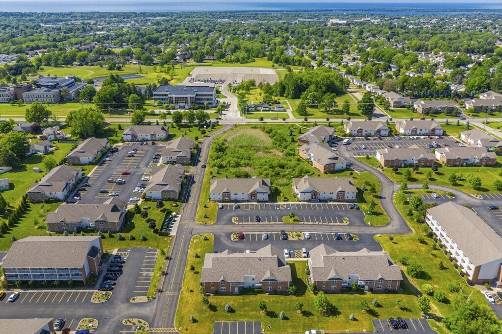 Aerial view of a residential area with multiple apartment buildings, parking lots, roads, and surrounding greenery on a clear day.