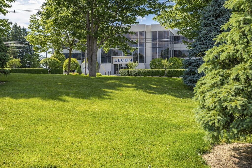 Large white building labeled "LECOM" surrounded by green trees and a grassy lawn.