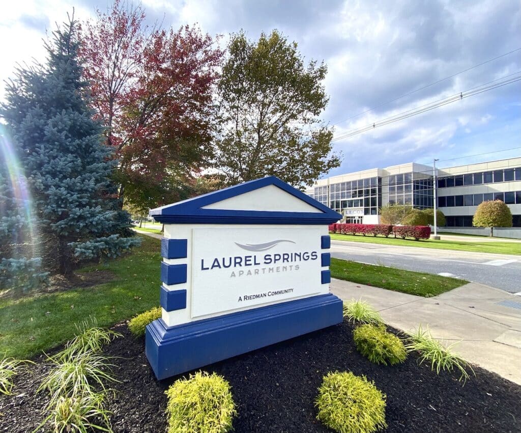 Sign for Laurel Springs Apartments next to a road, with trees and an office building in the background.