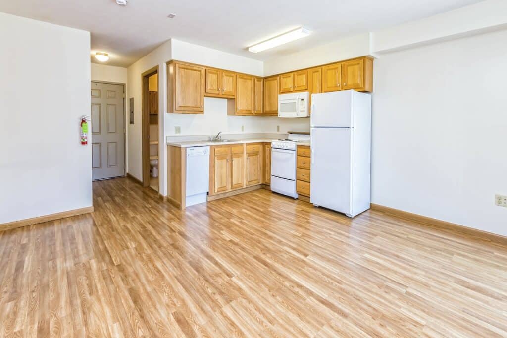 Kitchen with wooden cabinets, white appliances including refrigerator, stove, and microwave, and laminate wood flooring.
