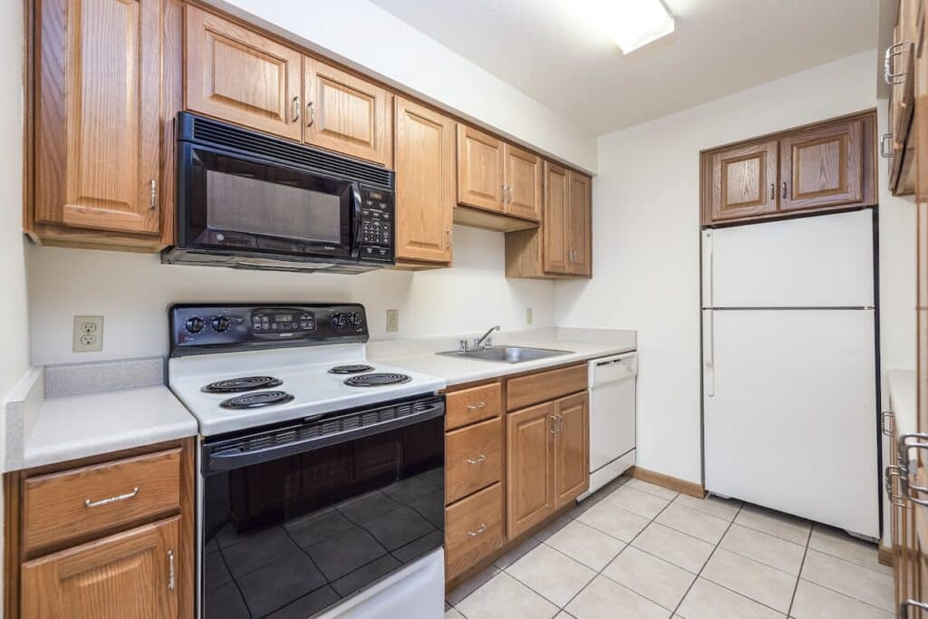 Kitchen with wooden cabinets, white appliances including a refrigerator, oven, and dishwasher, and a white countertop with a sink.