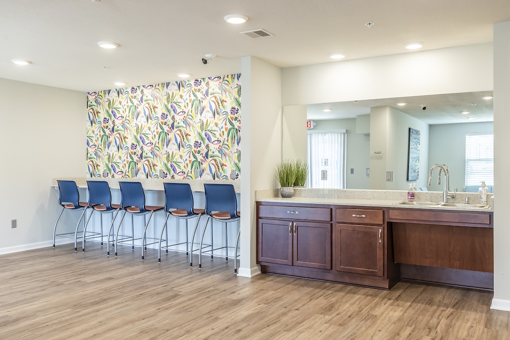 Study room with a floral patterned wall, bar stools, and a counter with a sink. The floor is LVP wood-look alike, and the area is well-lit with ceiling lights.