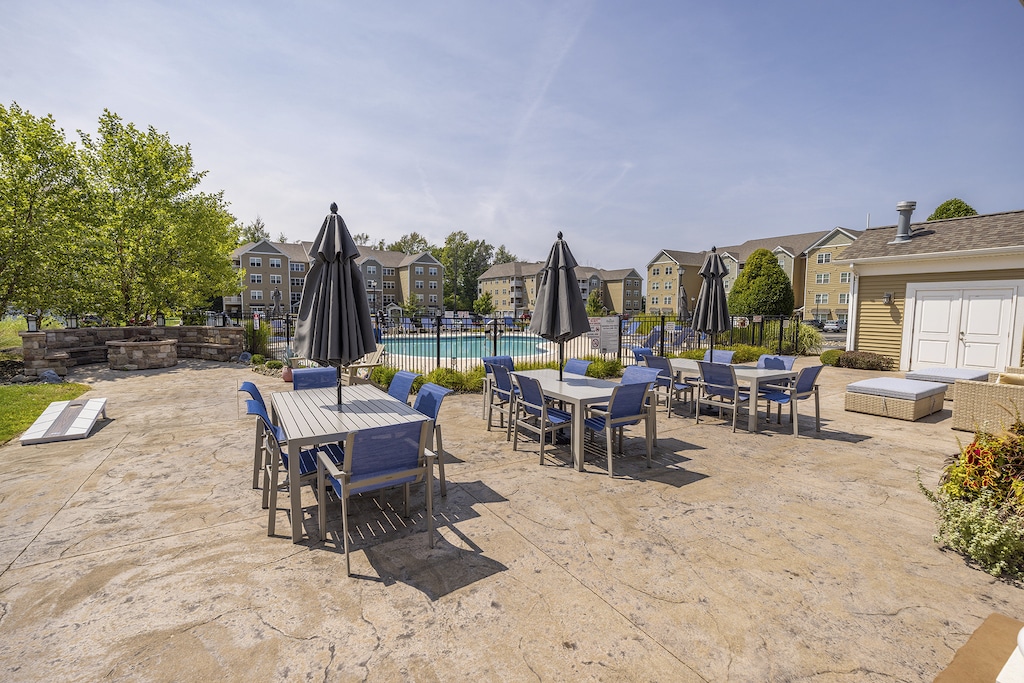 Outdoor patio with tables, blue chairs, and closed umbrellas. A fenced pool area is visible in the background.
