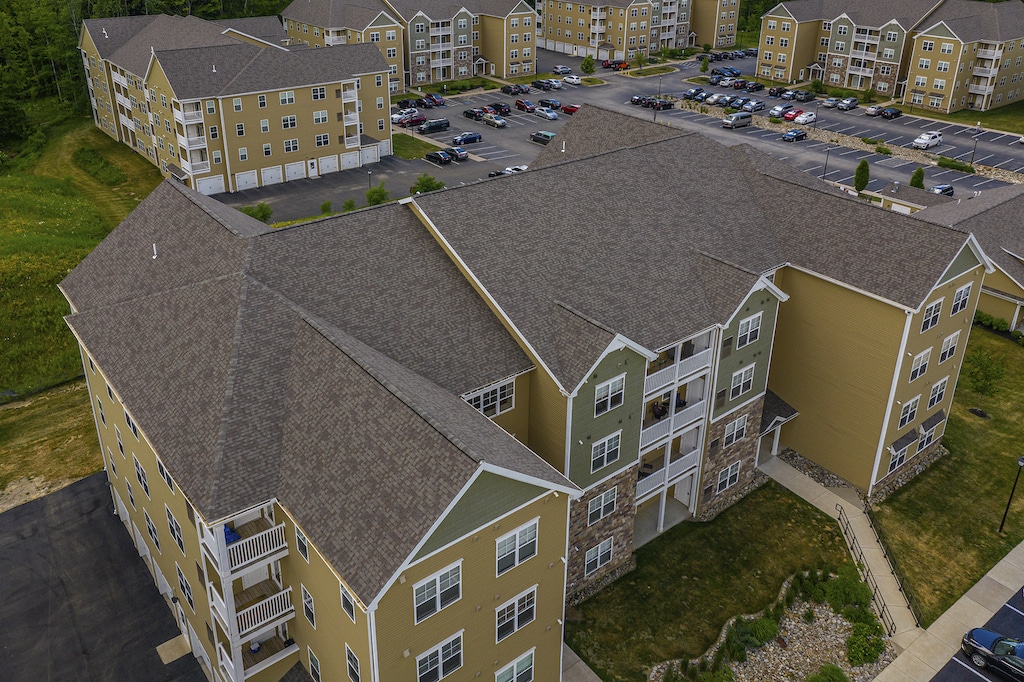 Aerial view of multiple apartment buildings with parking lots and cars, surrounded by greenery.