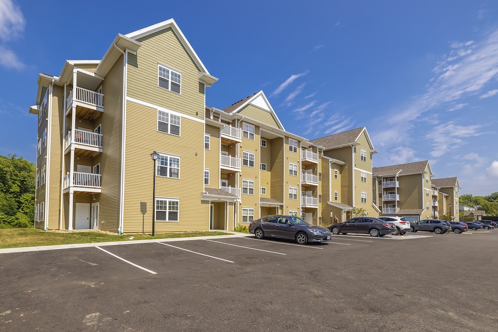 A row of modern apartment buildings with balconies, surrounded by a large parking lot.