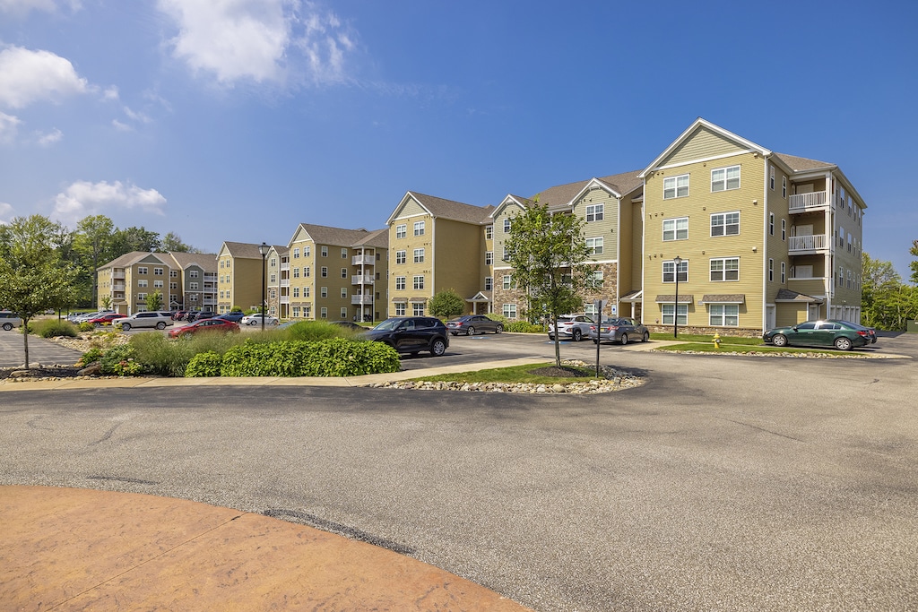 A row of beige, multi-story apartment buildings with balconies and green lawns.
