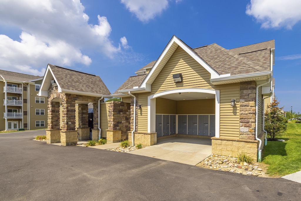 Mail and refuge center with stone pillars with trash compactor that sits next to a covered entrance a with attached mailbox units.