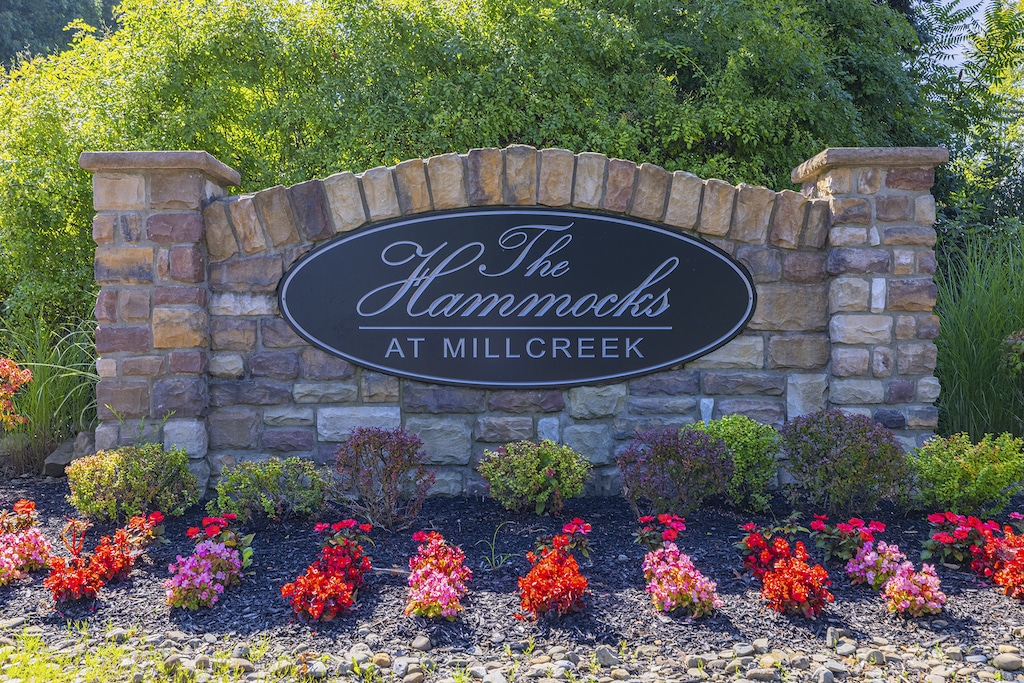 Stone entrance sign reads "The Hammocks at Millcreek" with flowers and shrubs in front.