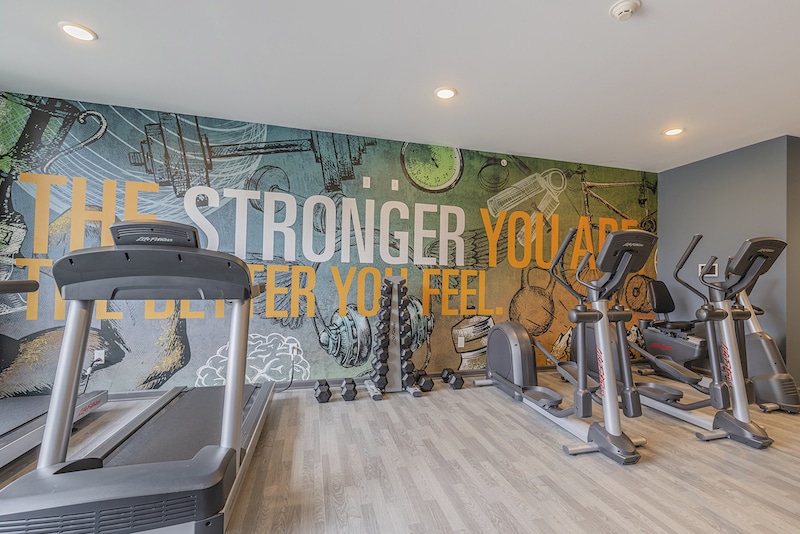 A gym with treadmills, ellipticals, and dumbbells. The wall has a colorful mural with motivational text.