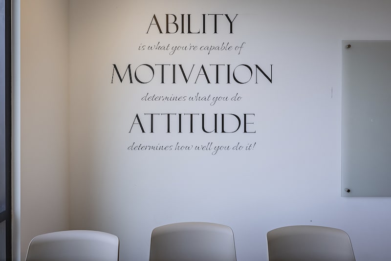 Wall with motivational quote about ability, motivation, and attitude above three empty chairs.