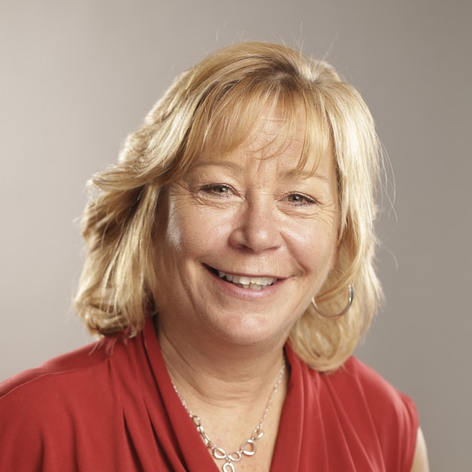 Smiling person with short blond hair wearing a red shirt and hoop earrings against a plain background.