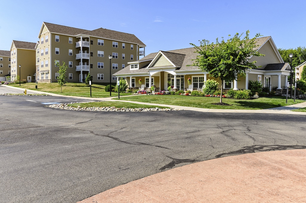 Apartment complex with multi-story buildings and a clubhouse, surrounded by greenery and a parking area under a clear blue sky.